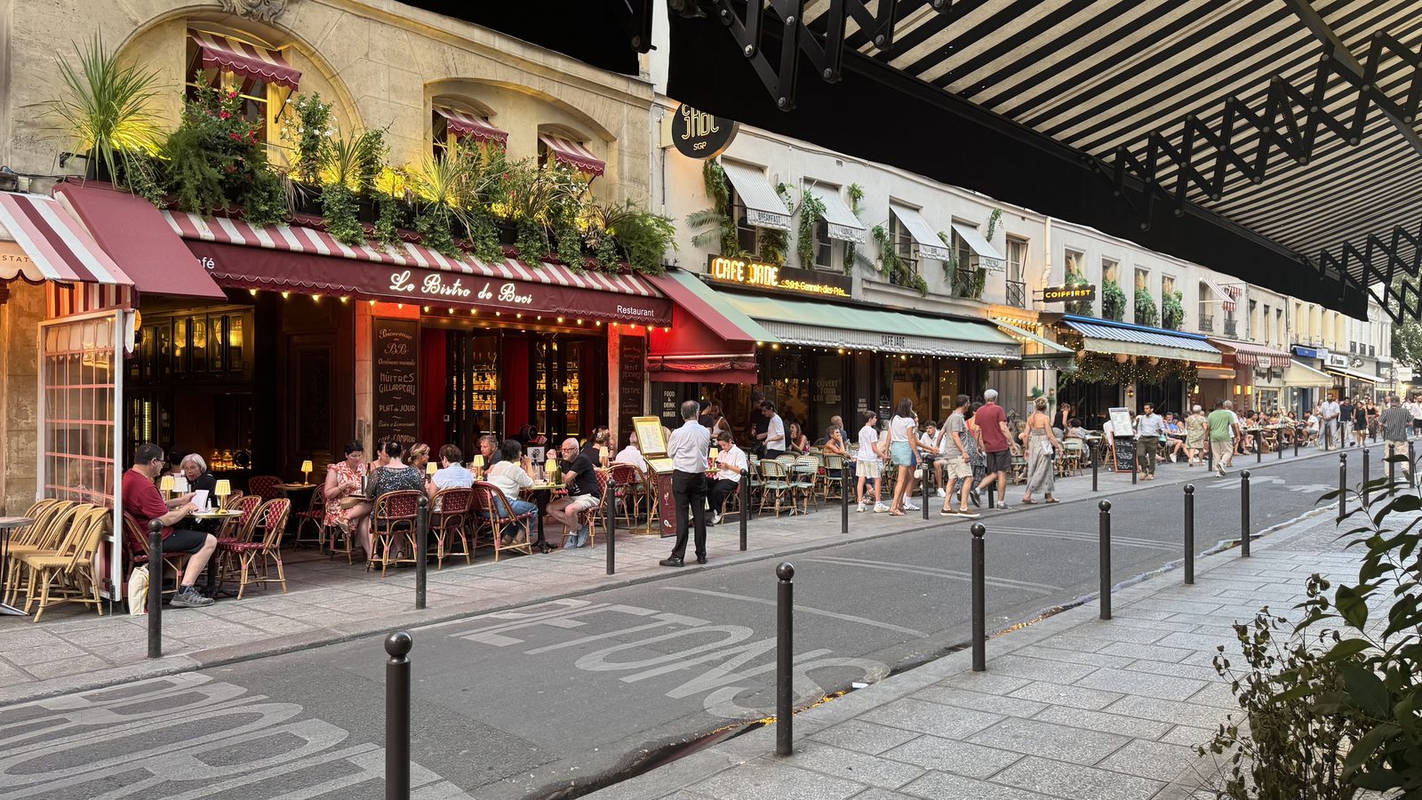 A lively Saint-Germain café street at golden hour, awnings and outdoor tables full of diners.