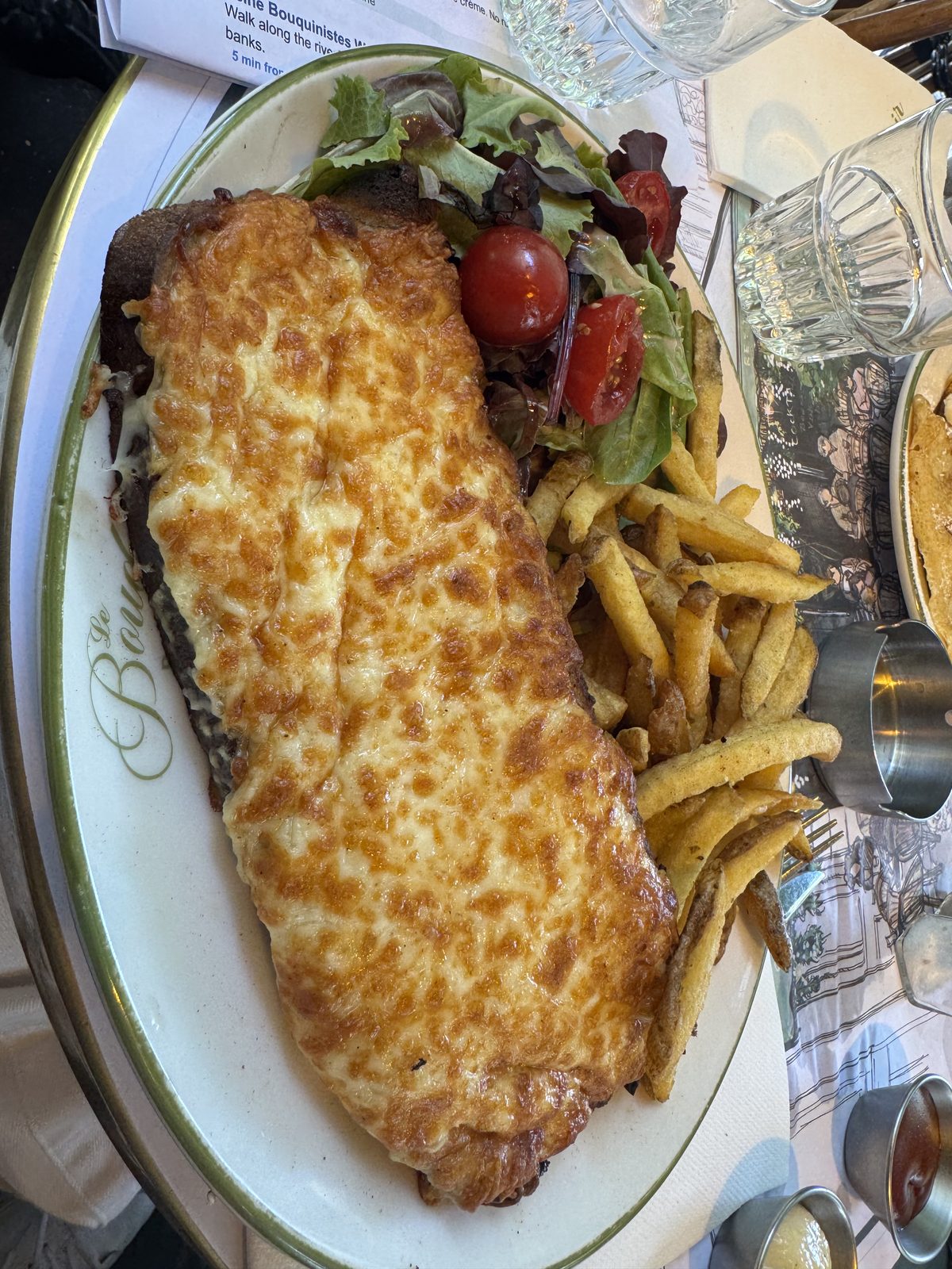 A golden, cheese-topped croque monsieur with salad and fries.