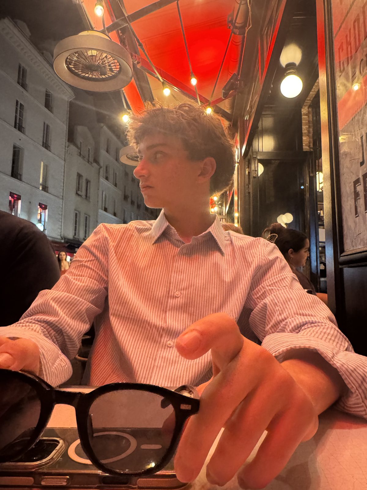 A teenager at a lamplit Paris café terrace at night.