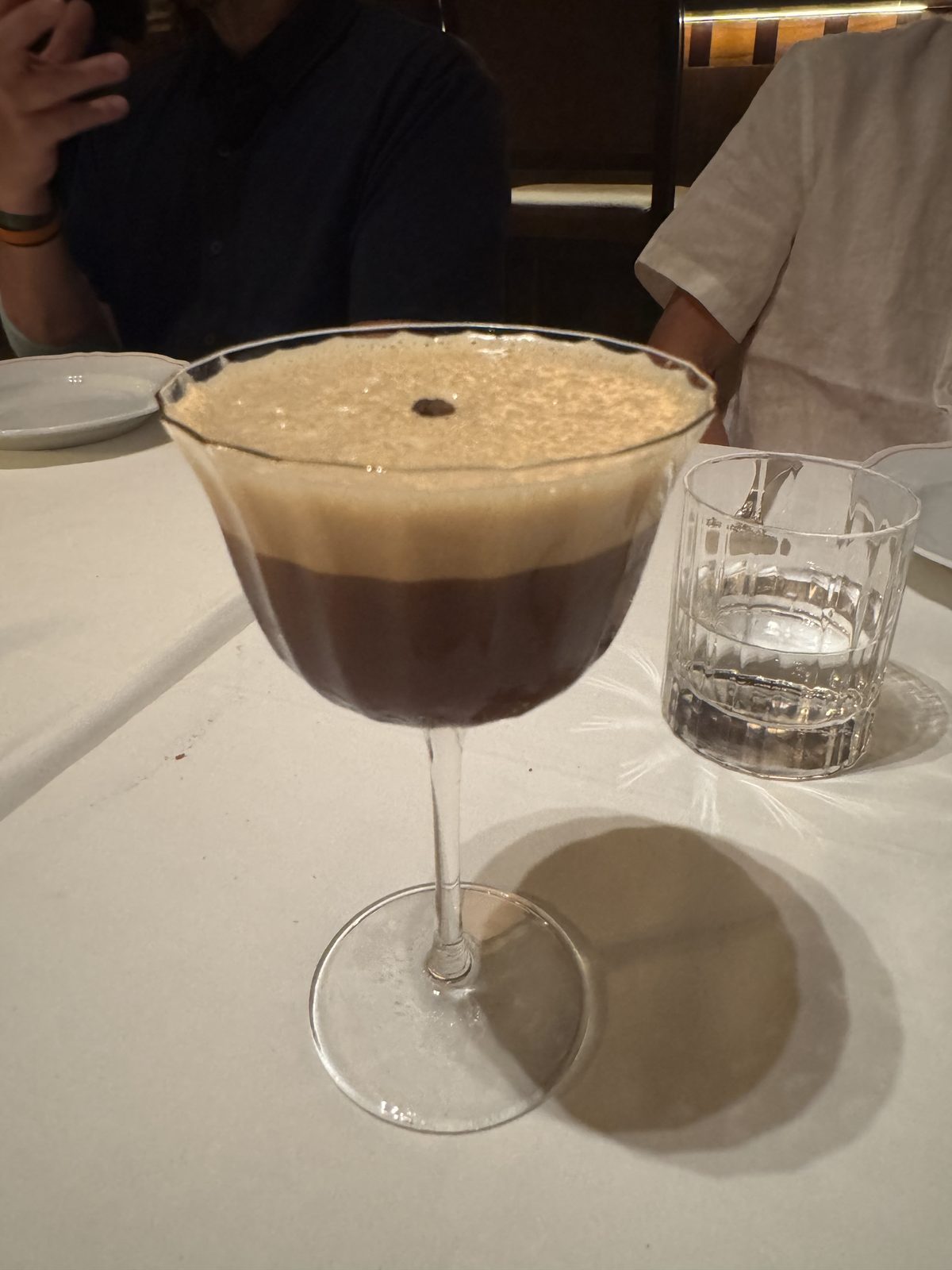 An espresso martini on a white tablecloth at dinner.